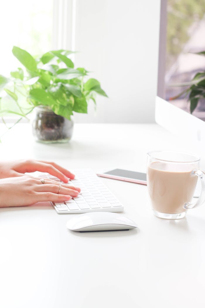 A woman working from home, typing on a keyboard with coffee nearby.
